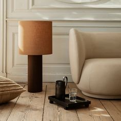 a table lamp sitting on top of a wooden floor next to a chair and ottoman