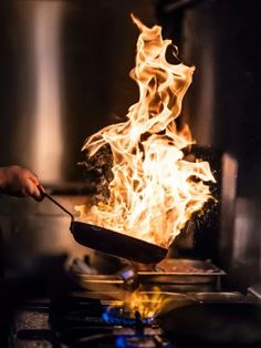 a person cooking food on top of a stove with flames in the background and a large pot full of hot coals