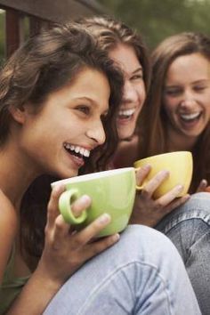 three girls laughing while holding coffee cups