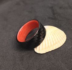 a black and red ring sitting on top of a shell next to a seashell