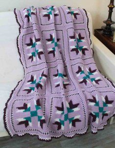 a purple crocheted blanket sitting on top of a bed next to a night stand