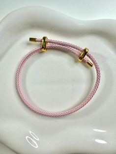 a pink rope bracelet with two gold clasps on a white ceramic plate, in the shape of a heart