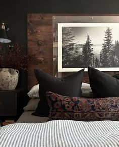 a bed with black and white pillows on top of it next to a wooden headboard