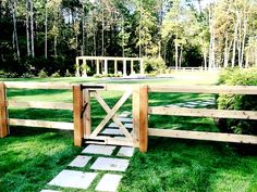 a wooden gate in the middle of a grassy area with stepping stones on it and a gazebo in the background