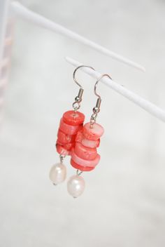 Introducing our exquisite Coral Stone & Big Freshwater Pearl Earrings, a captivating blend of elegance and craftsmanship. Handcrafted with precision using high-quality stainless steel, these unique earrings are a testament to meticulous artistry and attention to detail. The earrings feature a carefully curated selection of natural stones, adding a touch of authenticity to their design. Multiple stones are delicately threaded, creating a visually stunning composition. What makes these earrings truly stand out is the dangling freshwater pearl bead, elegantly swaying like a drop of liquid silver. With a length of 5.7cm (2.2 inches), these earrings are perfectly balanced, making them a versatile accessory suitable for various occasions. The combination of coral stone and freshwater pearl exude Handmade Mother Of Pearl Earrings For Wedding, Handmade Pearl White Dangle Pearl Earrings, Handmade Pearl White Drop Pearl Earrings, Handmade Pearl White Drop Earrings, Dangle Pearl Earrings For Gifts, Pearl Dangle Earrings As Gift, Pearl Dangle Earrings For Gift, Elegant Beaded Earrings With Pearl Charm For Gift, Pearl White Mother Of Pearl Dangle Earrings