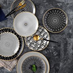 four black and white plates with gold rims on a gray tablecloth next to lemon slices