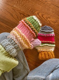 two knitted hats sitting on the floor next to someone's jeans and shoes