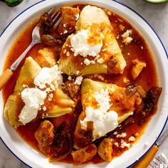 a white plate topped with dumplings covered in sauce and cheese next to a fork