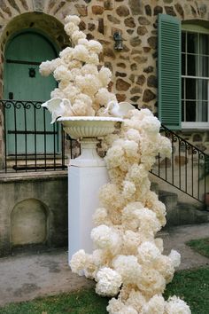 a white vase with flowers on top of it in front of a stone building