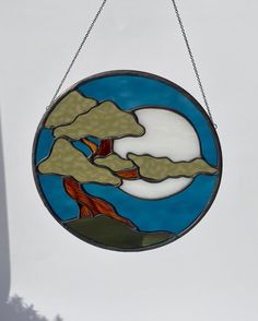 a stained glass window hanging from a chain on the side of a building with a tree in it