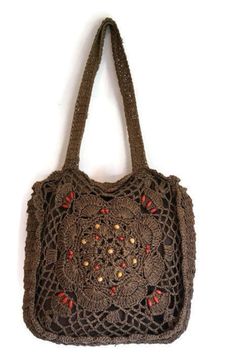 a brown crocheted bag hanging on a white wall with red beads and buttons