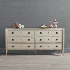 a white dresser with two vases on top of it next to a gray wall