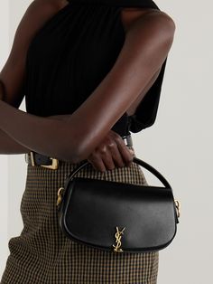 A practical investment piece, SAINT LAURENT's Italian-made 'Voltaire’ tote is crafted from buttery smooth black leather and punctuated with a signature gold-tone logo plaque. It has a short top handle and optional shoulder strap, which you can adjust to a comfortable drop. The compact, structured design is ideal for holding your phone, cardholder and lip gloss. Ysl Hat Outfit, Black Purse Designer, Ysl Bags, Yves Saint Laurent Bag, Ysl Handbags, Saint Laurent Tote, Gucci Eyewear, Bag Obsession, Yves Saint Laurent Bags