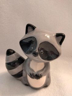 a ceramic raccoon figurine sitting on top of a snow covered ground