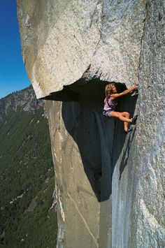 a woman climbing up the side of a large rock with her hands on her hips