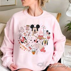 a woman sitting on top of a bed wearing a pink sweatshirt with mickey and minnie mouse