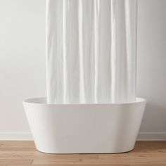 a white bathtub sitting on top of a wooden floor next to a shower curtain