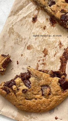 two chocolate chip cookies sitting on top of a piece of parchment paper next to each other