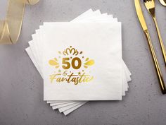 50 and fantastic napkins with gold foil on them next to forks, knife and fork