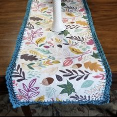 an ironing board covered in colorful leaves and crocheted trim on a wooden table