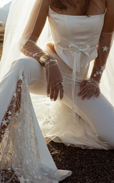 a woman in white is sitting on the ground wearing gloves and holding onto her dress