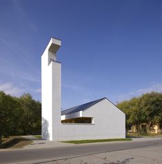 a white building with a black roof on the side and trees in the back ground