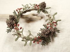 a wreath made out of pine cones and berries on a white tablecloth with a piece of wood in the background