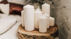 several white candles sitting on top of a wooden stand in front of a bed with pillows