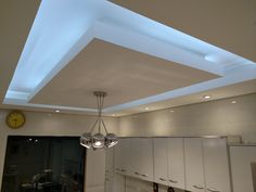 a kitchen with white cupboards and lights on the ceiling, and a clock in the background