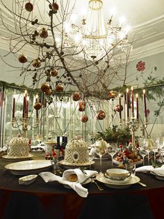 a dining room table is set for christmas with ornaments hanging from the chandelier