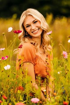 a beautiful blonde woman sitting in the middle of a field full of wildflowers