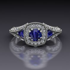 "Blue sapphires make a classic vintage style engagement ring. A round blue sapphire set in double prongs sits in a cushion-shaped diamond halo and blue sapphire trillions nestle in the split shank sides of this 14k white gold engagement ring with a bezel-set diamond on each side of the head. The top of the ring measures about 8.4mm at the widest point. The European shank at the bottom balances the whole ring out. Blue Sapphire Dimensions4.5mm EnhancementHeated ColorMedium to dark navy ClaritySli Classic Sapphire-colored Diamond Ring With Center Stone, Classic Blue Diamond Ring With Accents, Classic Sapphire Rings With Cushion Cut, Classic Blue Sapphire Ring With Diamond Accents, Classic Sapphire Halo Ring With Brilliant Cut, Classic Blue Halo Ring With Round Cut, Classic Sapphire Wedding Rings With Diamond Accents, Classic Blue Round Cut Halo Ring, Classic Blue Halo Ring