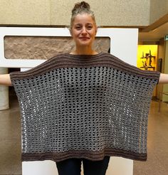 a woman is holding up a crocheted shawl