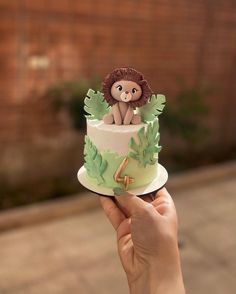 a hand holding a small cake decorated with a lion on the top and green leaves