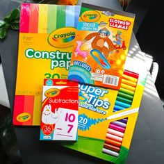 there are many different colored pencils and books on the table next to each other