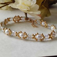 two bracelets with pearls and gold beads on top of a white table next to flowers