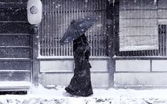 a woman walking down the street in the snow with an umbrella over her head while it's snowing