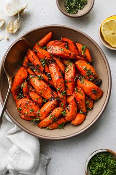 a bowl filled with cooked carrots next to bowls of herbs and lemon wedges