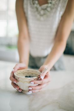 a woman is holding a white cup on a marble counter top with her hands in the bowl