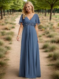 a woman in a blue dress standing on a dirt path