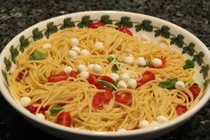 a white bowl filled with pasta topped with tomatoes and mozzarella sprinkled with green leaves