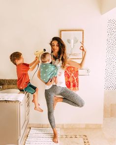 a woman holding a baby in her arms while standing next to a sink and mirror