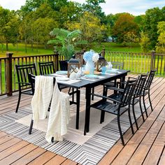 an outdoor table and chairs on a deck with flowers in vases, plates and napkins