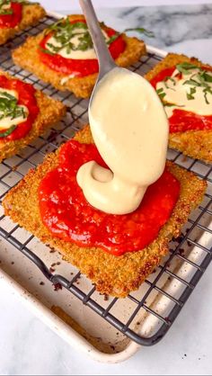 someone is dipping sauce on top of some small pizzas that are cooling on a rack