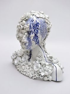 a white and blue sculpture with flowers on it's head, in the shape of a woman's head