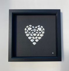 a black frame with white rocks in the shape of a heart hanging on a wall