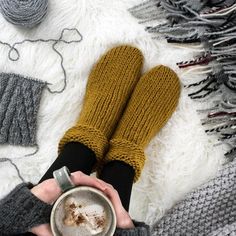 a person holding a cup of coffee in their hands on a rug with knitting supplies