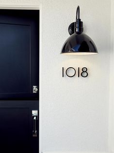 a black lamp hanging from the side of a white wall next to a door with an i108 sign on it