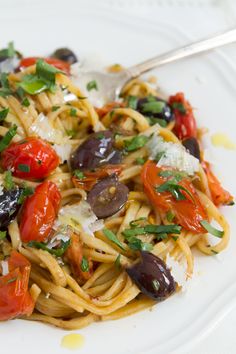 a plate of pasta with olives, tomatoes and parmesan cheese on it