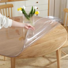 a person holding a vase with flowers in it on top of a round wooden table